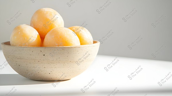An image of a ceramic bowl in a light cream color, containing five frozen balls in an apricot hue. The balls are placed inside the bowl, with natural light reflecting on them, giving a soft and refreshing feel.