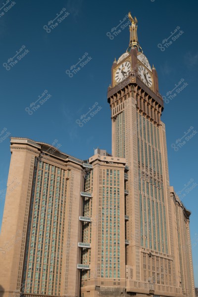 Image of the Clock Tower in Mecca, Saudi Arabia. The tall building features modern architecture with a large clock at the top, set against a clear blue sky.