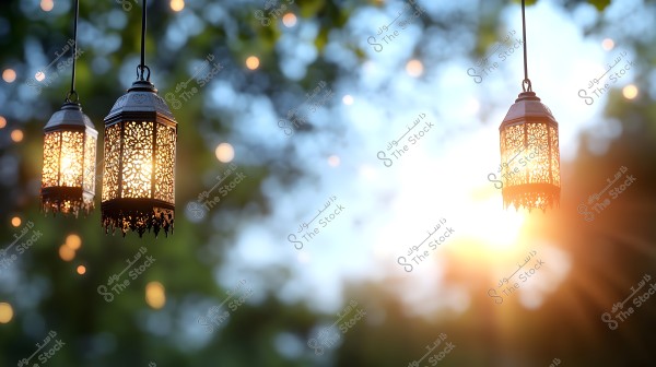 Three traditional Arabic lanterns hang from above, each intricately designed with decorative patterns and illuminated from within. The lanterns are set against a blurred outdoor background featuring scattered small lights and greenery, with the sun glowing in the distance.