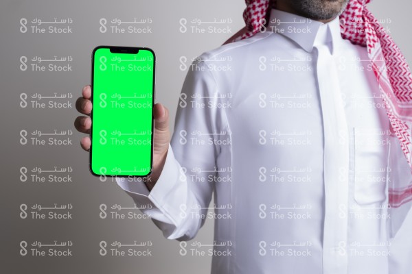 صورة ملتقطة بهاتف لرجل سعودي يرتدي الزي السعودي التقليدي يمسك بالجوال ويعرض شاشته بوضوح