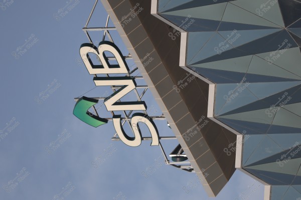 Image shows the \"SNB\" logo in green and white on the side of a modern building with a distinctive geometric design consisting of glass facade and sharply defined angles under a blue sky.
