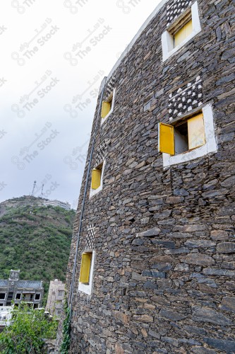 An ancient building built of medium stones, windows surrounded by white paint while the sky looks cloudy at sunset, Rijal Almaa heritage village in the Asir region