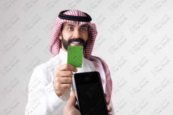 Portrait of a Saudi man holding a card and making automatic payments on a white background