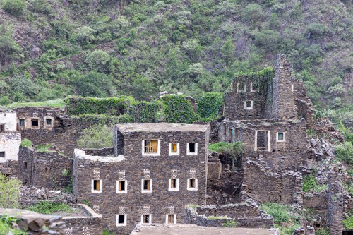 An ancient building built of stones in the middle of a group of windows surrounded by white paint while the sky looks cloudy during sunset, Rijal Almaa Heritage Village in the Asir region