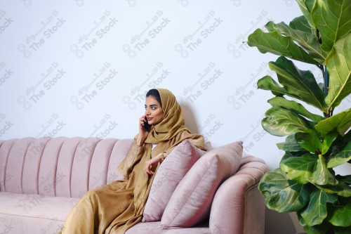 A Saudi girl sitting on the sofa and making different expressions using a mobile phone