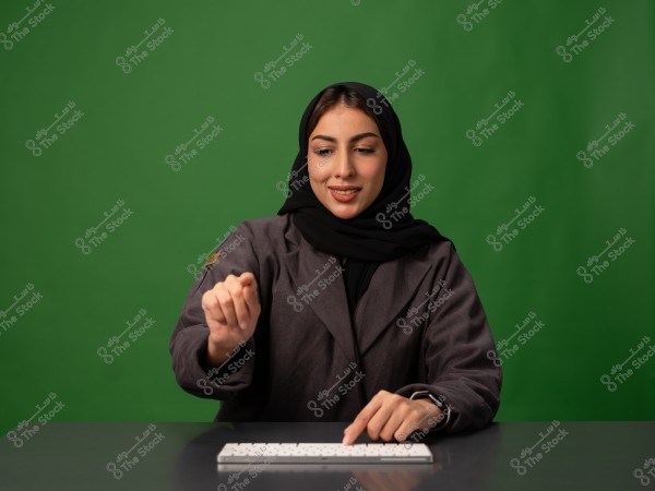 امرأة ترتدي حجاباً تعمل على لوحة مفاتيح مع خلفية خضراء.