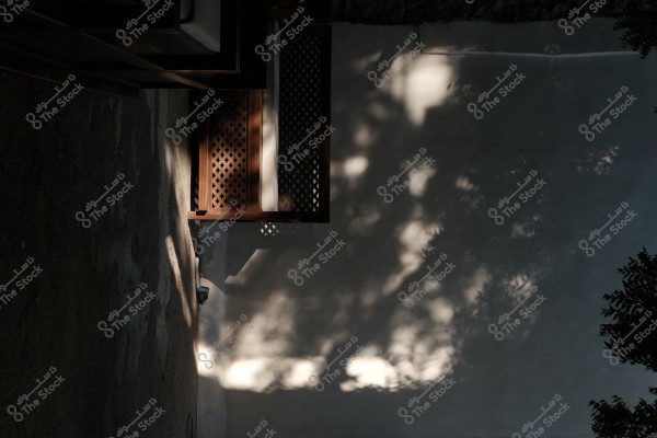 Shadows of trees on a white wall next to an ornate wooden window.