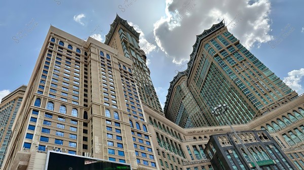 Image of the facade of the Abraj Al Bait hotels under the blue sky with clouds in Mecca.