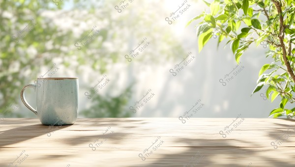 A light blue ceramic mug sits on a wooden table in daylight. In the background, green leaves of a tree are illuminated by the sunlight, creating a calm and natural atmosphere in the image.