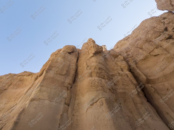 صورة تظهر قمة جبل صخري بني اللون تحت سماء زرقاء صافية. تبدو الصخور سلسة في بعض المناطق مع تفاصيل بارزة في أجزاء أخرى, مما يبرز التشكيل الطبيعي للنتوءات الصخرية.

-