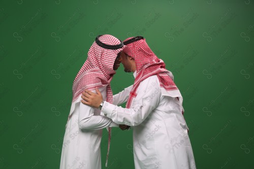 Portrait of two Saudi men in traditional uniform on a green background shaking hands smiling, sad, angry, memorial photos, documenting a happy moment.