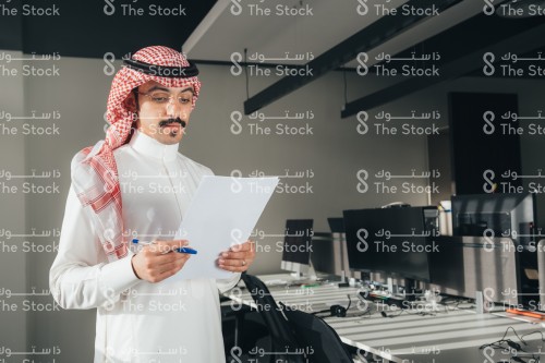 موظف سعودي يرتدي الثوب في العمل ويحمل اوراق بيديه.