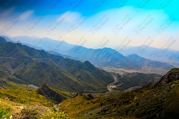 A snapshot of a series of towering rocky mountains and paved roads extending in the Al Hada Mountains in Taif, showing a cloudy sky during the day, mountain heights, Taif Mountains, mountain range