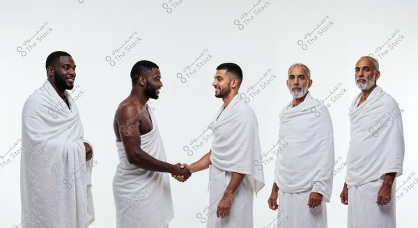 The image features a group of five men, all dressed in traditional white Ihram garments worn by Muslims during the pilgrimage of Hajj or Umrah. Two of the men are shaking hands, while the others stand beside them. The attire consists of two pieces of unstitched white cloth wrapped around the body.