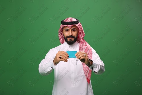 رجل سعودي على خلفية خضراء مبتسم يحمل بطاقة الصراف جاهز للتسوق.