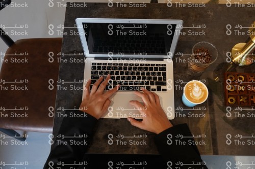 شاب سعودي يعمل ويستخدم جهاز محمول في المقهى وبجابنه كوب قهوة