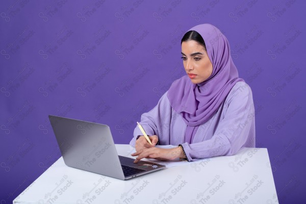 Portrait of a young Saudi woman wearing an abaya and hijab, holding a pen and thinking, against a purple background