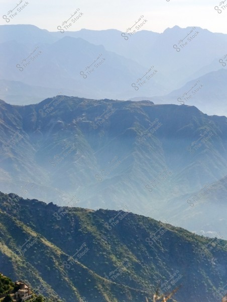 The image shows a series of mountains adorned with green vegetation at the lower part of the picture, and a cascade of misty ridges and valleys fading into the background. The horizon is clearly visible with a clear sky and distant mountains blending into the skyline.