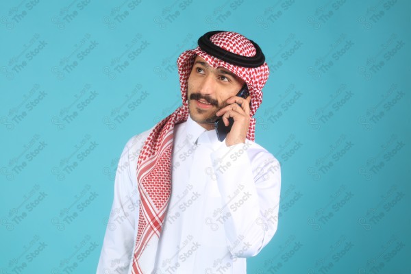 بورتريه رجل يرتدي الزي السعودي على خلفية تركوازية، يتحدث بهاتفه وتبدوا على ملامحة السعادة، الاتصالات والتقنية