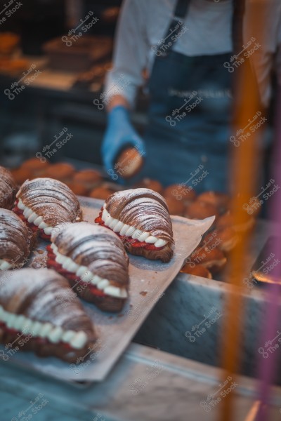 Display of chocolate croissants filled with cream and strawberries at a bakery, with a person wearing a blue glove in the background.