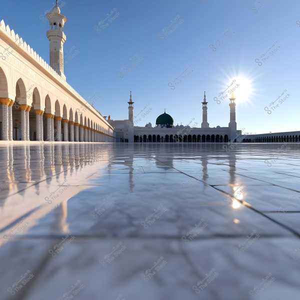 The image shows a beautiful view of the courtyard of the Prophet\'s Mosque in Medina, Saudi Arabia. In the background, the mosque\'s distinctive green dome is visible along with two tall minarets on each side. The expansive courtyard is paved with reflective white tiles that mirror the bright sunlight during either sunrise or sunset.