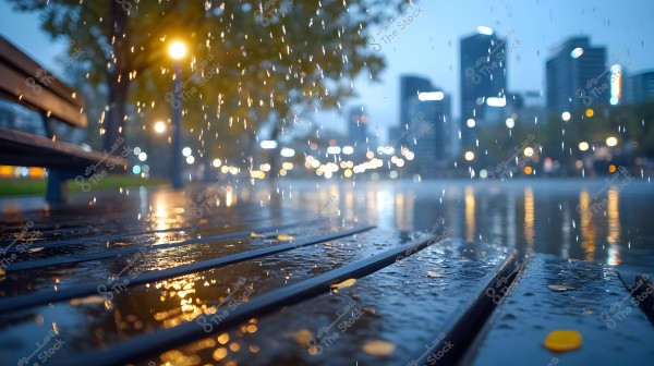 An image of a wooden bench in a park under the rain, with blurry city lights reflecting on the wet ground in the background. Some fallen leaves are visible on the bench and the wet pavement.