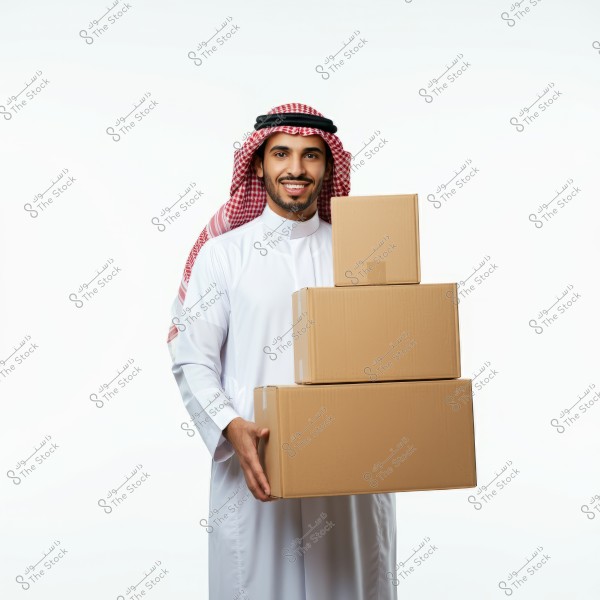 A man wearing traditional Saudi attire featuring a thobe, ghutra, and aqal, is holding three cardboard boxes of varying sizes. The man is smiling and standing against a white background.
