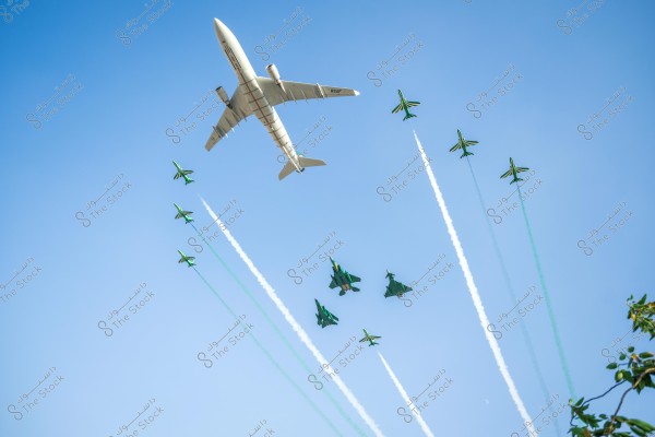 A large passenger airplane flies in the blue sky accompanied by a formation of green fighter jets emitting white and green smoke. The large airplane is marked with \"Royal Saudi Air Force,\" and the fighter jets fly in an organized formation, creating a stunning aerial display. Some green leaves are visible in the lower right corner of the image.