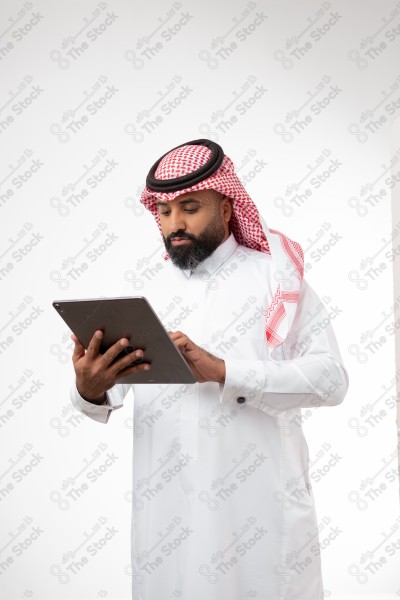 بورتريه رجل سعودي يحمل بيده الآيباد و ينظر لشاشته ويقوم بتعابير مختلفة، خلفية بيضاء