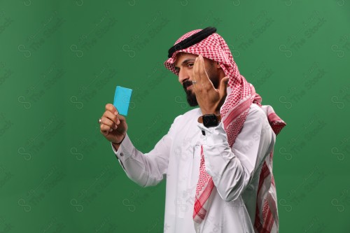 بورتريه رجل سعودي على خلفية خضراء متحمس يحمل بطاقة الصرافة مستعد للتسوق