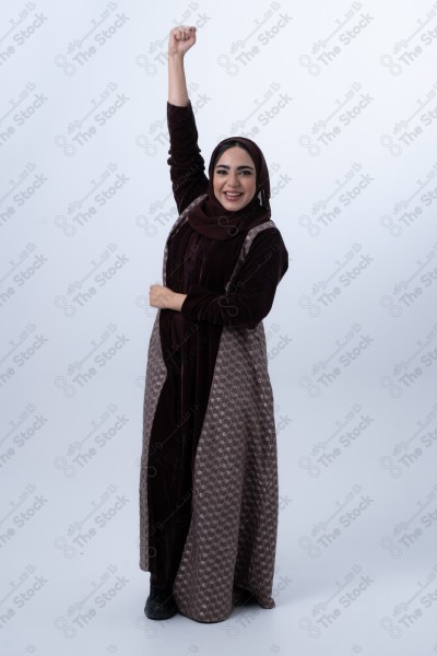 Portrait of a young Saudi woman wearing an abaya and hijab, with a smiling facial expression, standing against a white background