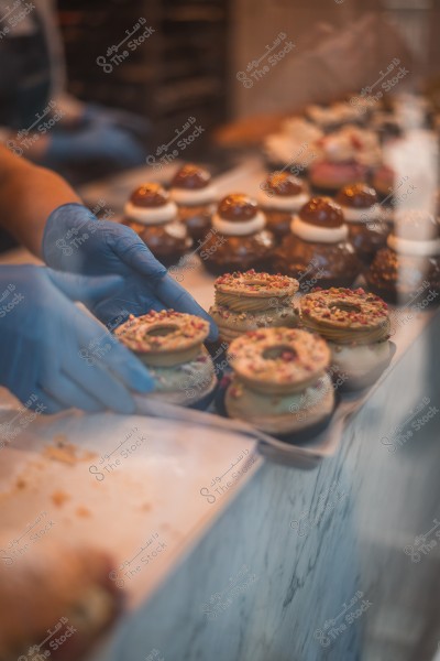 A person wearing blue gloves arranging decorated pastries on a display table in a shop.