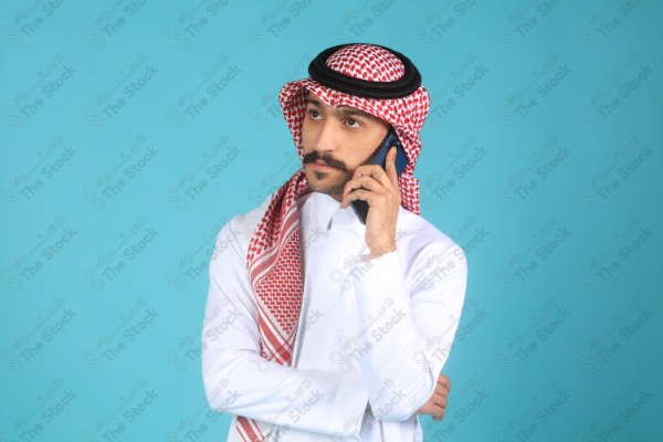 بورتريه رجل يرتدي الزي السعودي على خلفية تركوازيه، يتحدث بهاتفه وتبدوا على ملامحة السعادة، الاتصالات والتقنية