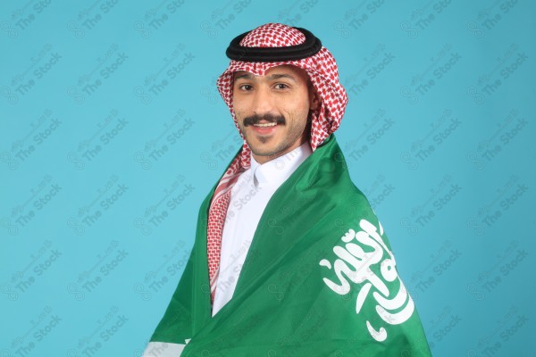 A young Saudi man wearing the Saudi dress and holding the Saudi flag makes expressions of happiness and enthusiasm, Saudi flag