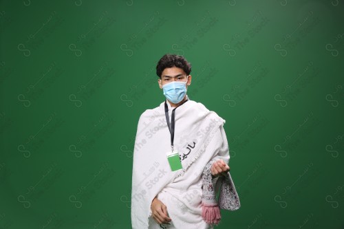 Portrait of a pilgrim with white skin on a green background, wearing Ihram to perform Hajj, carrying a prayer rug