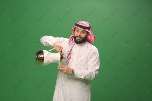 شاب سعودي على خلفية خضراء يرتدي الثوب و الشماغ، يقوم بعمل حركات بيده، يصب القهوه السعودية، احتفالات العيد