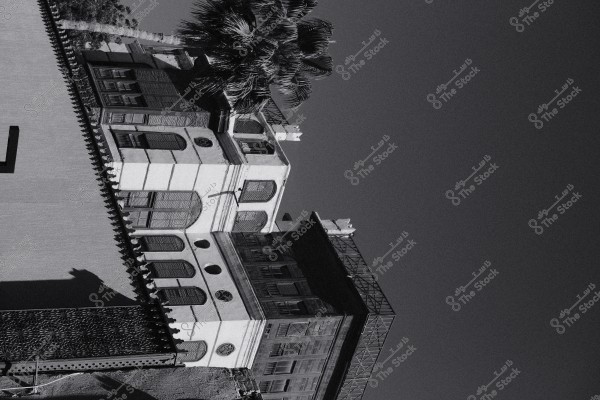 A historical building with traditional architecture style featuring wooden windows and palm trees in the background in a black and white image.