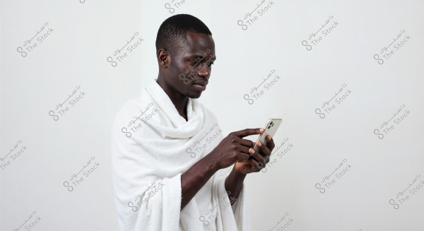 A person wrapped in a white towel looks at a smartphone in their hand. The background is plain white and clean.