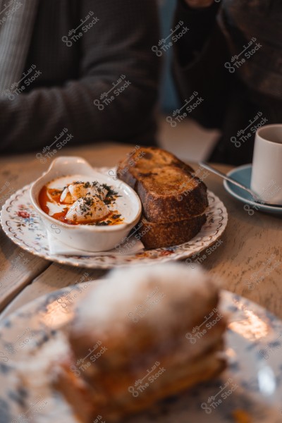 A dish of poached eggs with sauce and spices next to slices of toasted bread on a wooden table with a cup of drink.