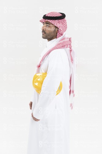 بورتريه صورة مقربة من الجانب لمهندس سعودي يرتدي الزي السعودي ويحمل تحت ذراعه خوذة المهندسين على خلفية بيضاء.