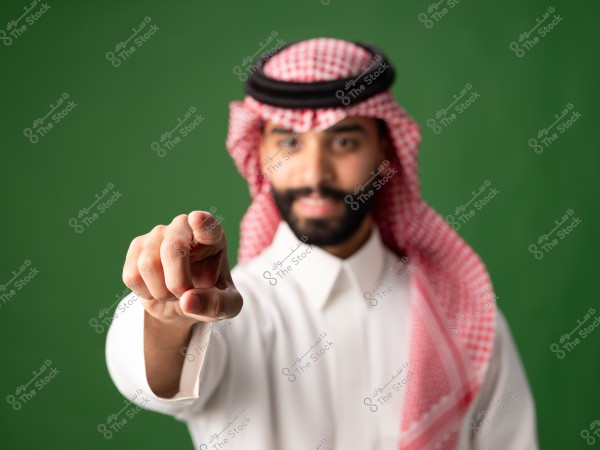 صورة لرجل يرتدي الزي التقليدي السعودي, يشتمل على الثوب الأبيض والغترة الحمراء مع العقال الأسود, يقف أمام خلفية خضراء. الرجل تظهر ملامحه ضبابية بينما يوجه إصبعه نحو الكاميرا مما يعطي إحساساً بالتفاعل المباشر.