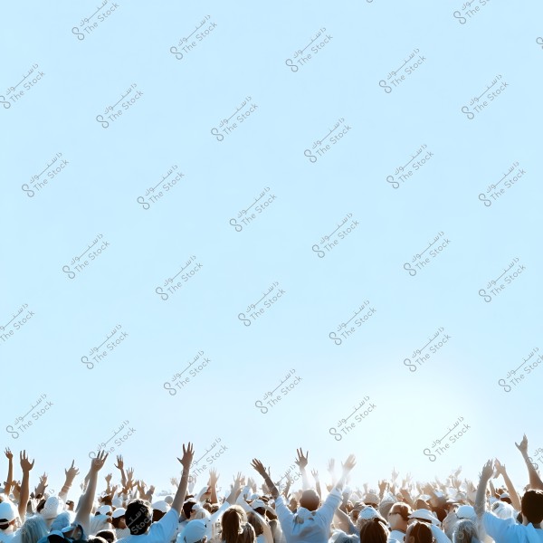 A crowd of people wearing white clothing, raising their hands towards the sky in a festive outdoor atmosphere. The sky is clear blue, adding a sense of freedom and joy.