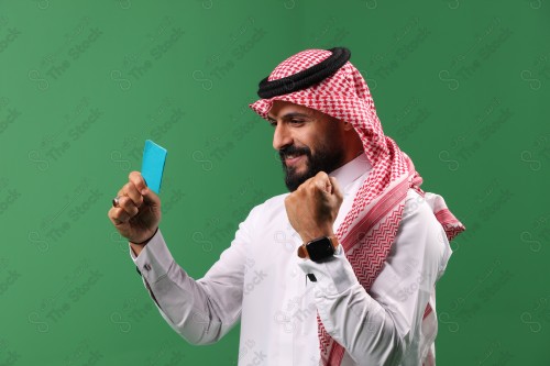 بورتريه رجل سعودي على خلفية خضراء متحمس يحمل بطاقة الصرافة مستعد للتسوق