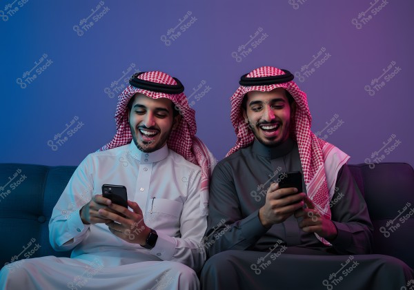 A portrait of two Saudi Arabian men sitting on a couch. Both are wearing traditional thobes and ghutras, one in white and the other in gray. They are smiling and looking at their smartphones in a relaxed setting with blue and pink lighting in the background.