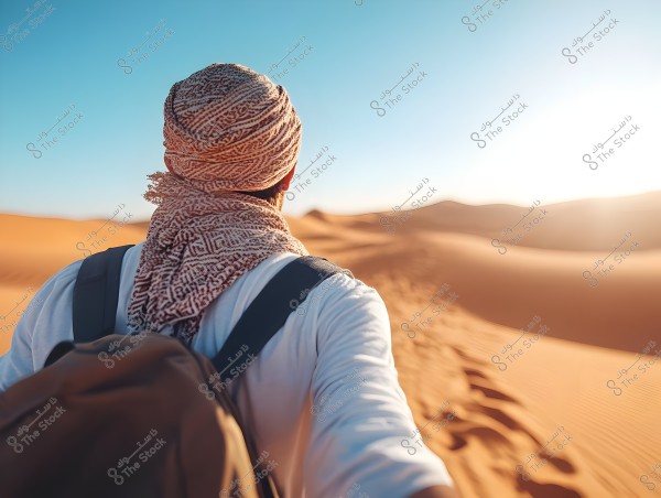 An image of a man walking in the desert under the bright sun. He is wearing a white headscarf with red patterns and a keffiyeh on his head, a white shirt, and carrying a backpack. Behind him, expansive sand dunes are visible under a clear blue sky.\r\n\r\n3. **Provide relevant