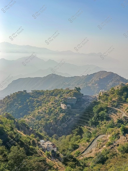 A beautiful landscape depicting a series of mountains shrouded in mist, with small houses and stone walls arranged on agricultural terraces on the hillsides. A road is visible winding through the lush terrain, with a clear blue sky in the background.