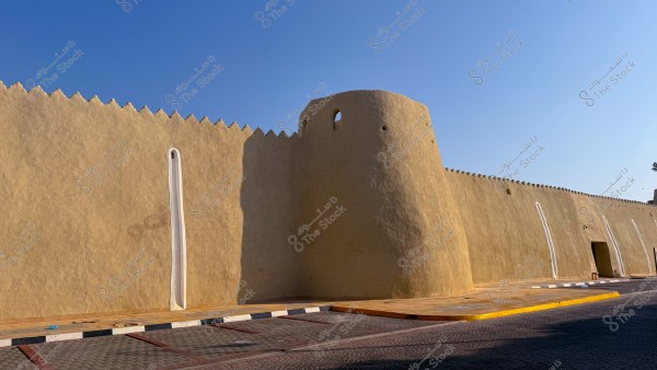 Image of a large beige fortress wall with a small round tower, on a sunny day with clear blue skies.