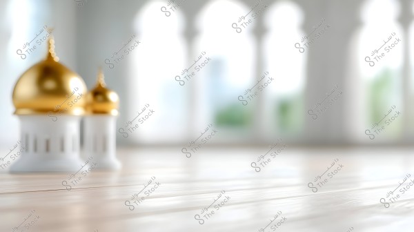 Image of a mosque interior with white and gold furnishings. In the foreground, there are two small models of mosque domes in gold atop white bases. The background features large white columns and arches, slightly blurred.
