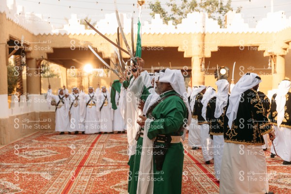 رجال سعوديون يرتدون الزي التقليدي يؤدون رقصة العرضة النجدية في قرية مبنية على الطراز التراثي