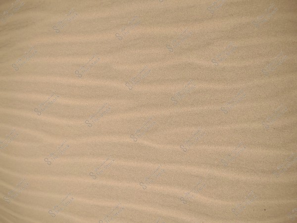 The image shows desert sand with a wavy pattern, where the sand dunes create harmonious lines shaped by the wind. The sand is soft and uniform in color, with shades of light brown.